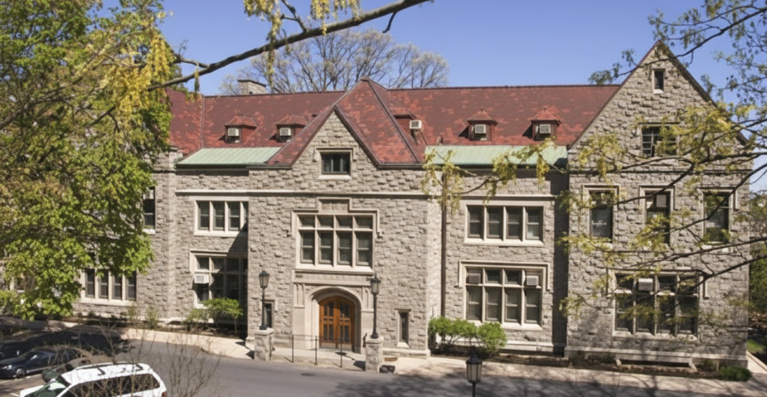 Stone building with red roof surrounded by trees.
