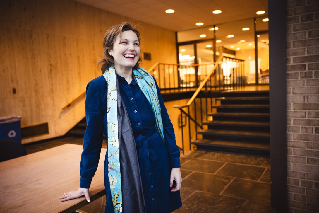 Liz Barrett stands in front of steps wearing a dark blue dress and looking at the camera.